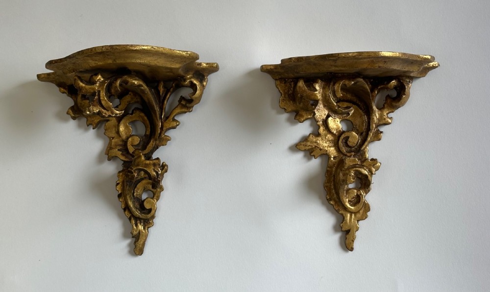 A pair of carved wood wall brackets with a hand-gilded gold finish featuring acanthus leaf scrollwork and flat top shelves. View V