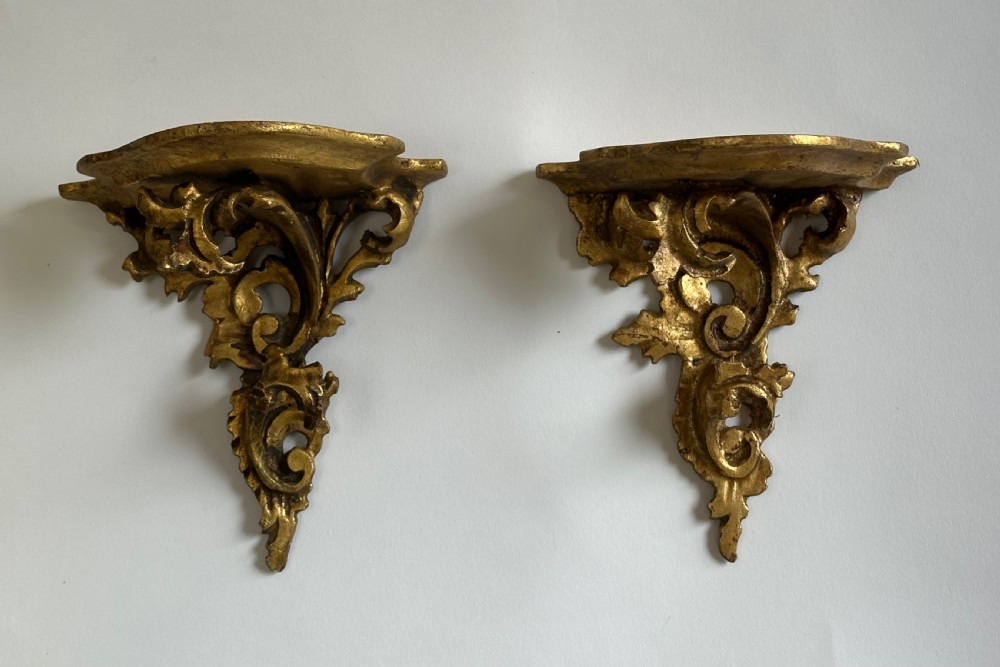 A pair of carved wood wall brackets with a hand-gilded gold finish featuring acanthus leaf scrollwork and flat top shelves. View IX