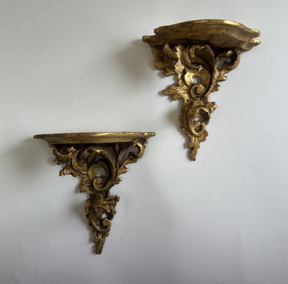 A pair of carved wood wall brackets with a hand-gilded gold finish featuring acanthus leaf scrollwork and flat top shelves. View XIII