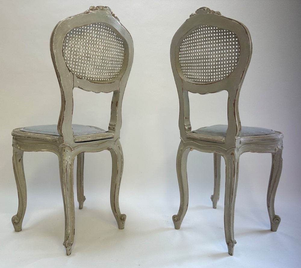 A pair of French Louis XV style side chairs with distressed grey painted frames, woven cane oval backrests, and grey fabric upholstered seats. View III