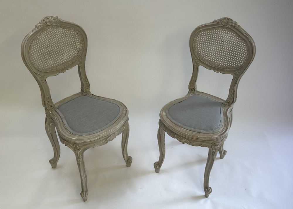 A pair of French Louis XV style side chairs with distressed grey painted frames, woven cane oval backrests, and grey fabric upholstered seats. View IV