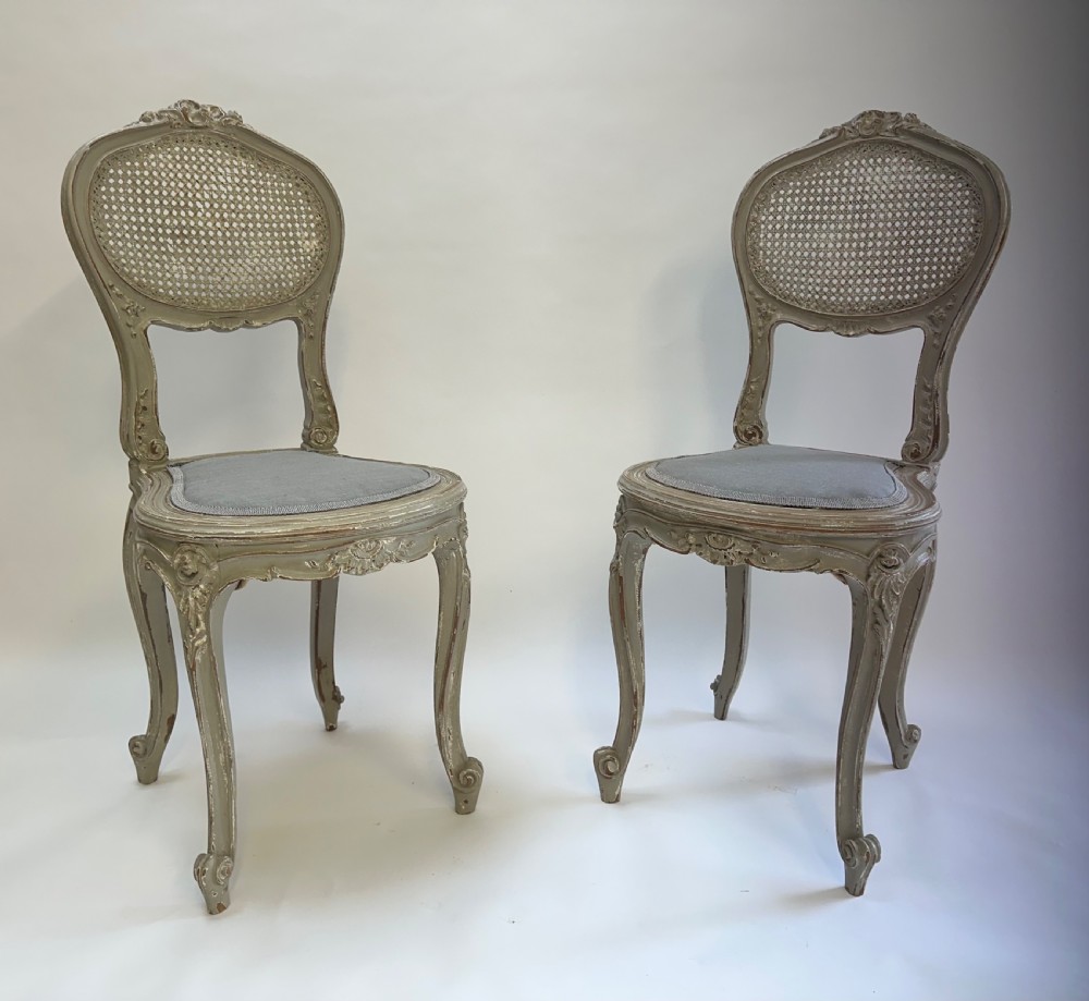 A pair of French Louis XV style side chairs with distressed grey painted frames, woven cane oval backrests, and grey fabric upholstered seats. View V
