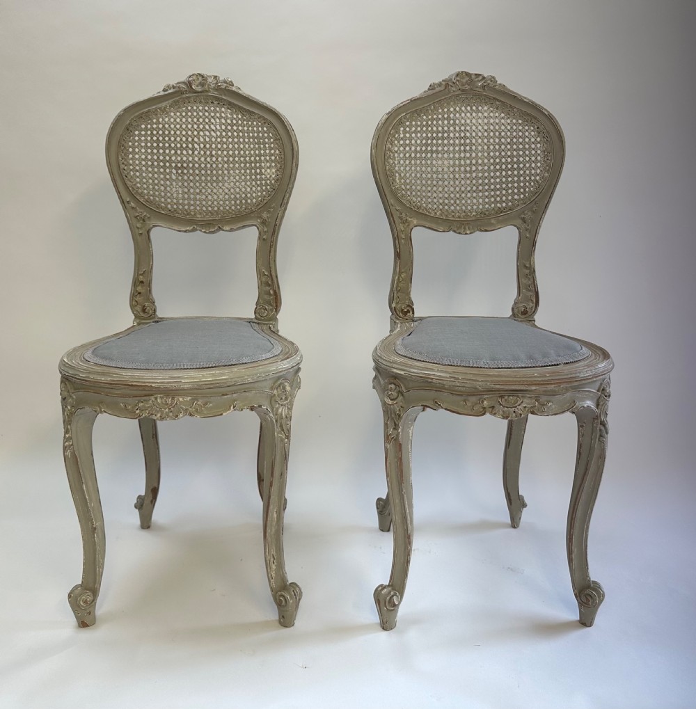 A pair of French Louis XV style side chairs with distressed grey painted frames, woven cane oval backrests, and grey fabric upholstered seats. View VI