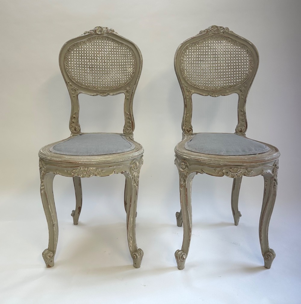 A pair of French Louis XV style side chairs with distressed grey painted frames, woven cane oval backrests, and grey fabric upholstered seats. View VII