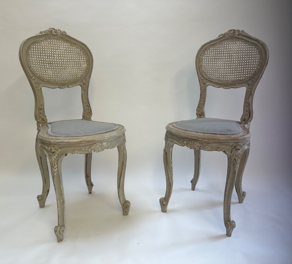 A pair of French Louis XV style side chairs with distressed grey painted frames, woven cane oval backrests, and grey fabric upholstered seats. View VIII