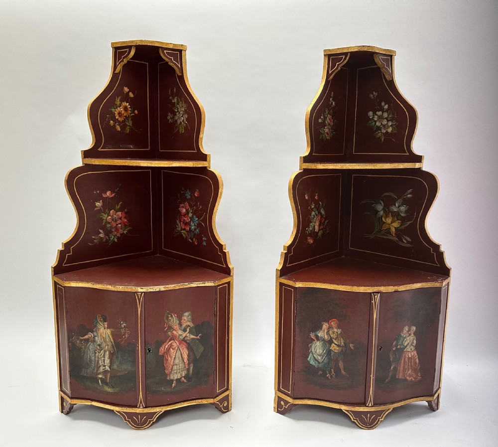 A matching pair of deep burgundy and gold painted Italian corner cupboards with upper open shelves and lower cabinet doors featuring hand-painted figures.