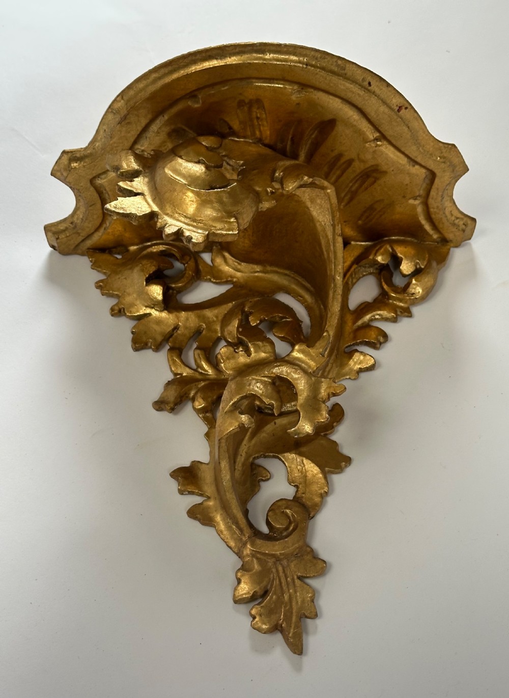 An Italian carved wood wall bracket featuring ornate acanthus leaf scrollwork with a gilded gold leaf finish supporting a semi-circular shelf top. View II