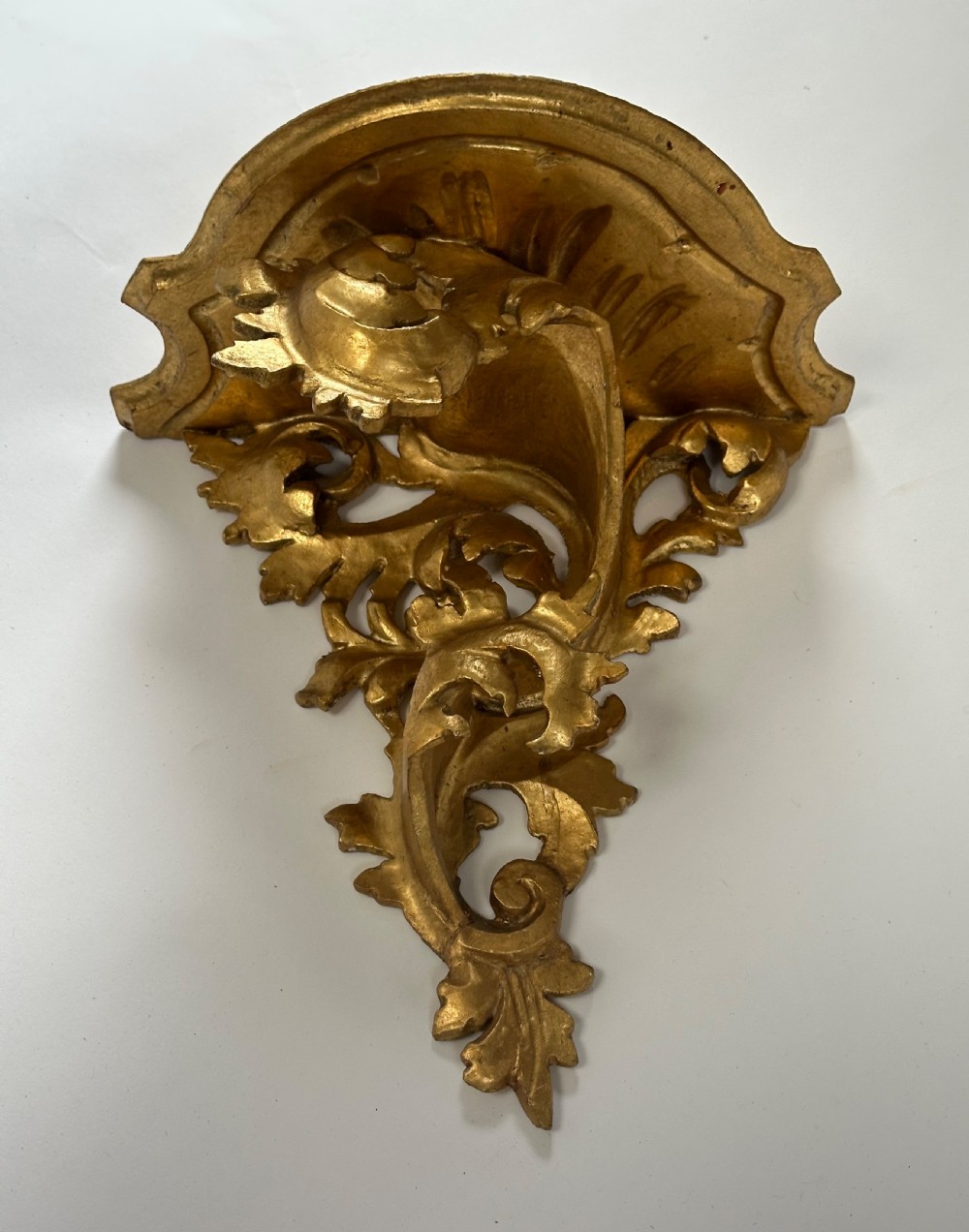 An Italian carved wood wall bracket featuring ornate acanthus leaf scrollwork with a gilded gold leaf finish supporting a semi-circular shelf top. View V