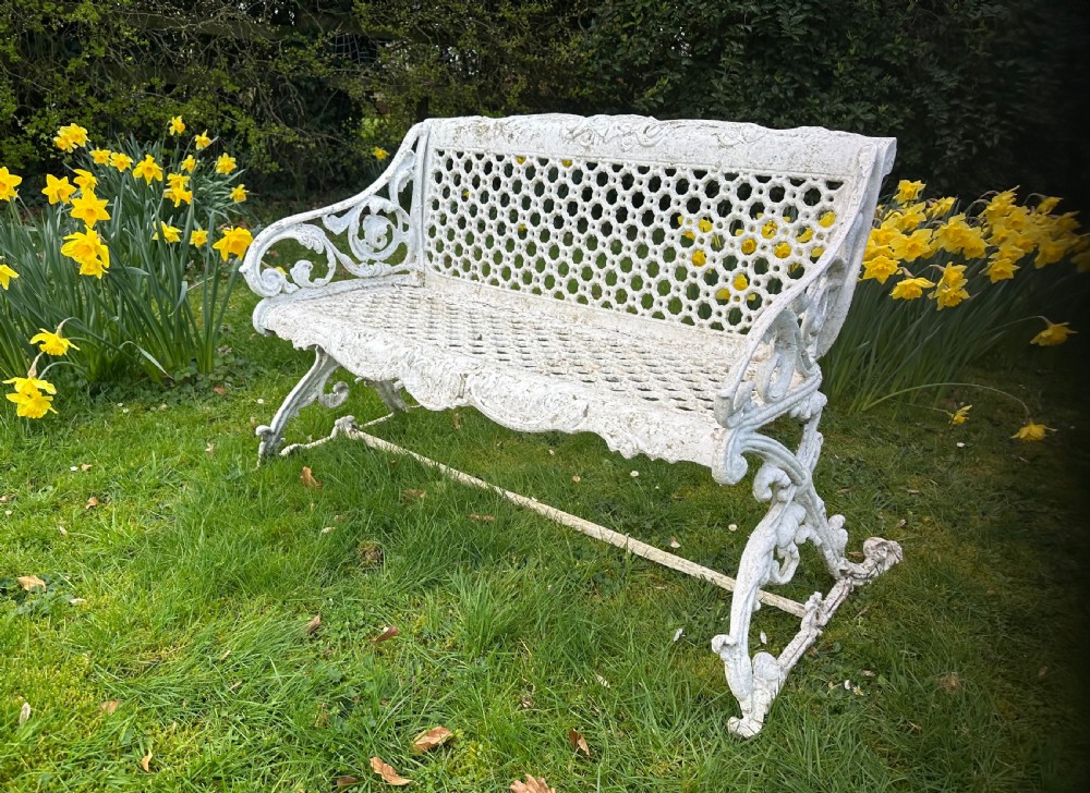 A Victorian white painted cast iron garden bench featuring a pierced lattice backrest and ornate scrolled armrests.