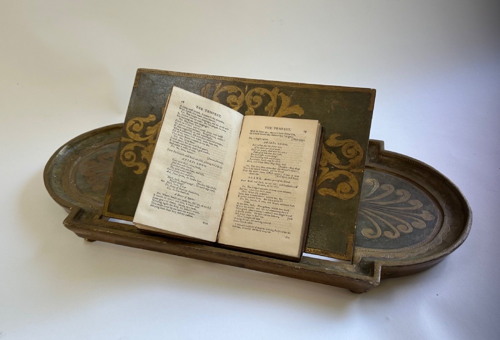 An antique Florentine painted and giltwood tabletop book stand with an open book resting on its angled surface.