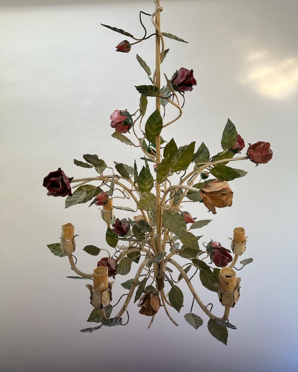 A French painted metal chandelier featuring dark green leaves, red rose blossoms, and cream candle-style lamp holders.