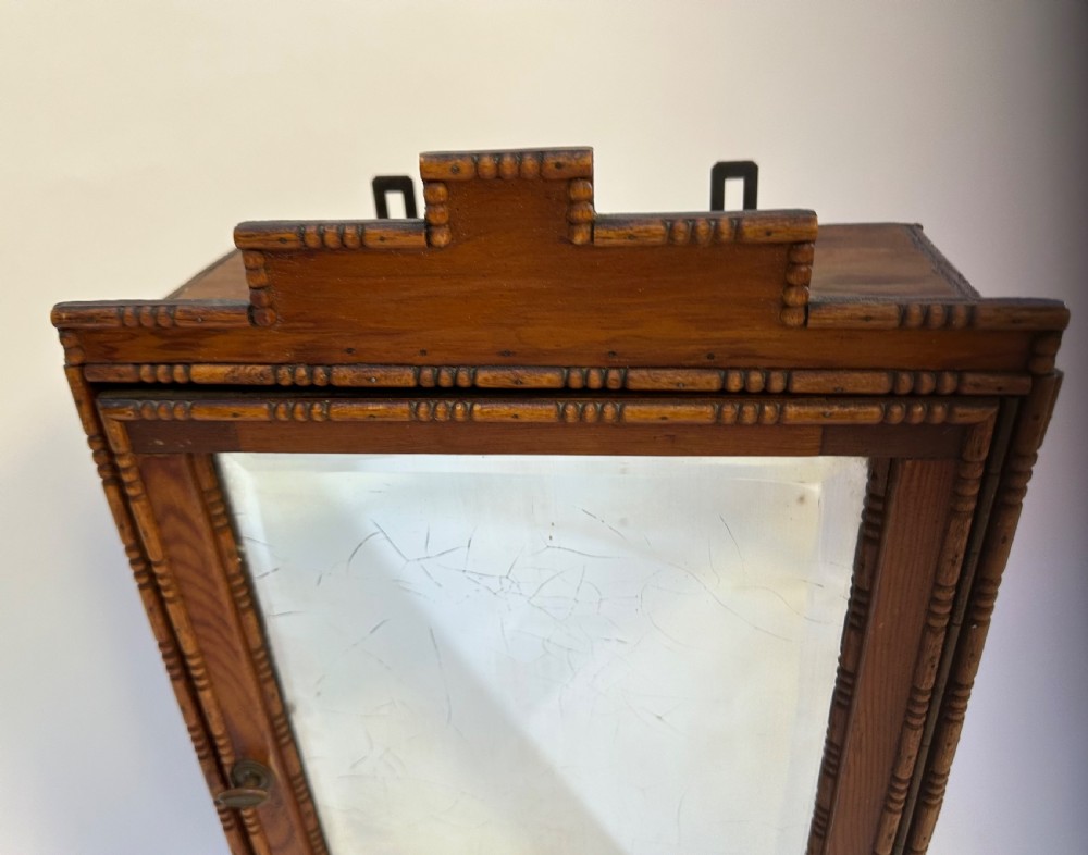 A small warm brown wooden French cabinet featuring a bevelled glass mirror door, bobbin moulding borders, a stepped pediment crest, and a lower drawer. View IV
