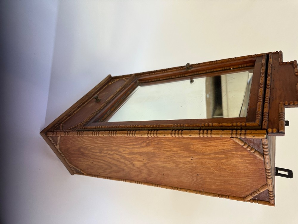 A small warm brown wooden French cabinet featuring a bevelled glass mirror door, bobbin moulding borders, a stepped pediment crest, and a lower drawer. View VI