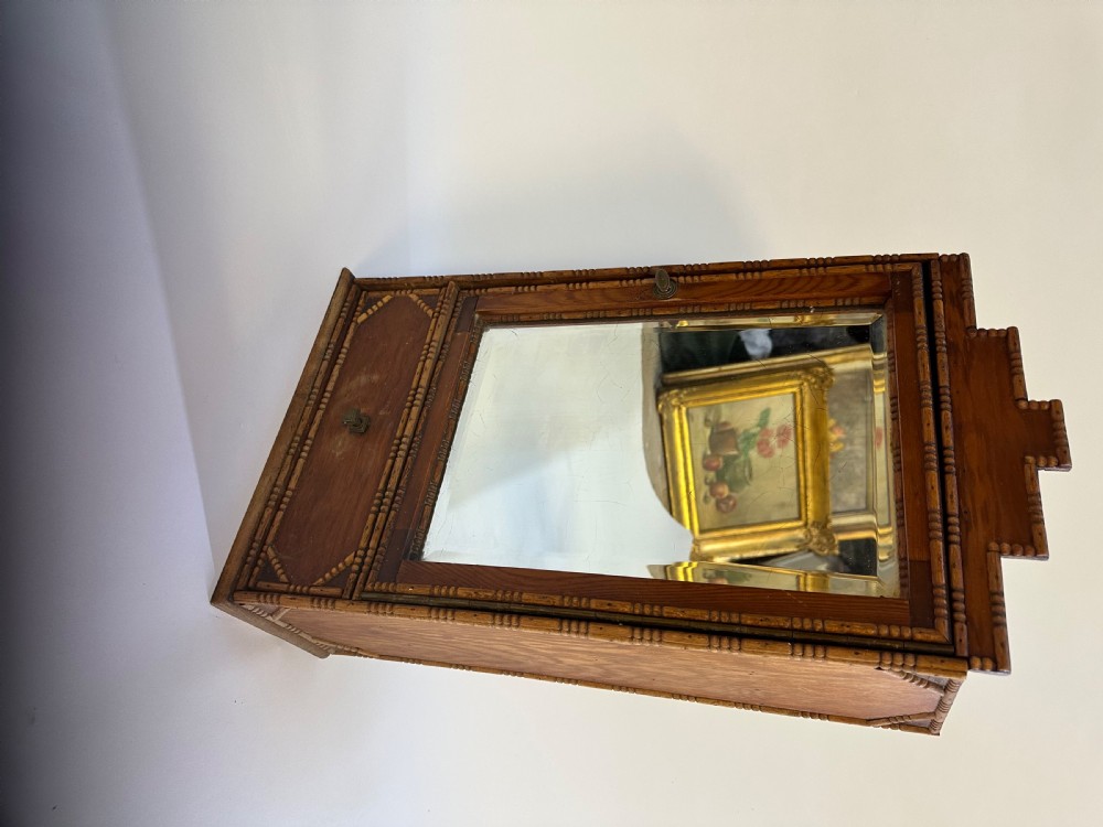 A small warm brown wooden French cabinet featuring a bevelled glass mirror door, bobbin moulding borders, a stepped pediment crest, and a lower drawer. View VII