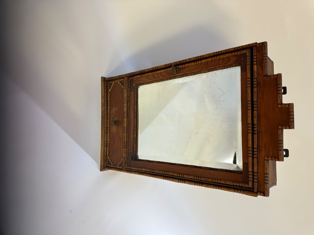 A small warm brown wooden French cabinet featuring a bevelled glass mirror door, bobbin moulding borders, a stepped pediment crest, and a lower drawer. View VIII