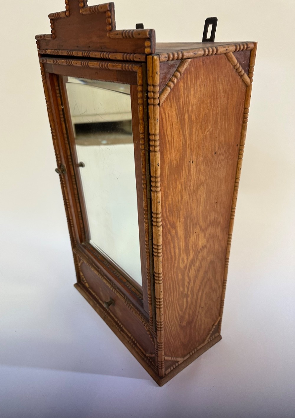 A small warm brown wooden French cabinet featuring a bevelled glass mirror door, bobbin moulding borders, a stepped pediment crest, and a lower drawer. View IX
