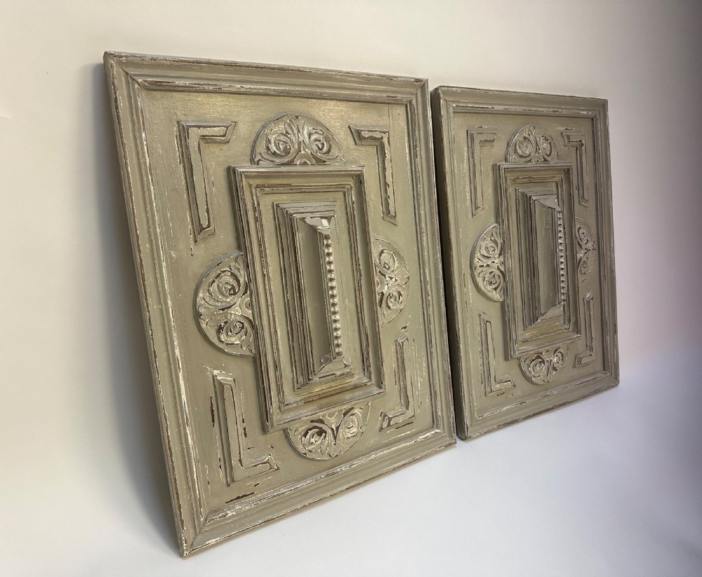 A pair of rectangular French hand-carved wooden panels featuring raised geometric mouldings, relief scrolls, and a distressed grey painted finish.