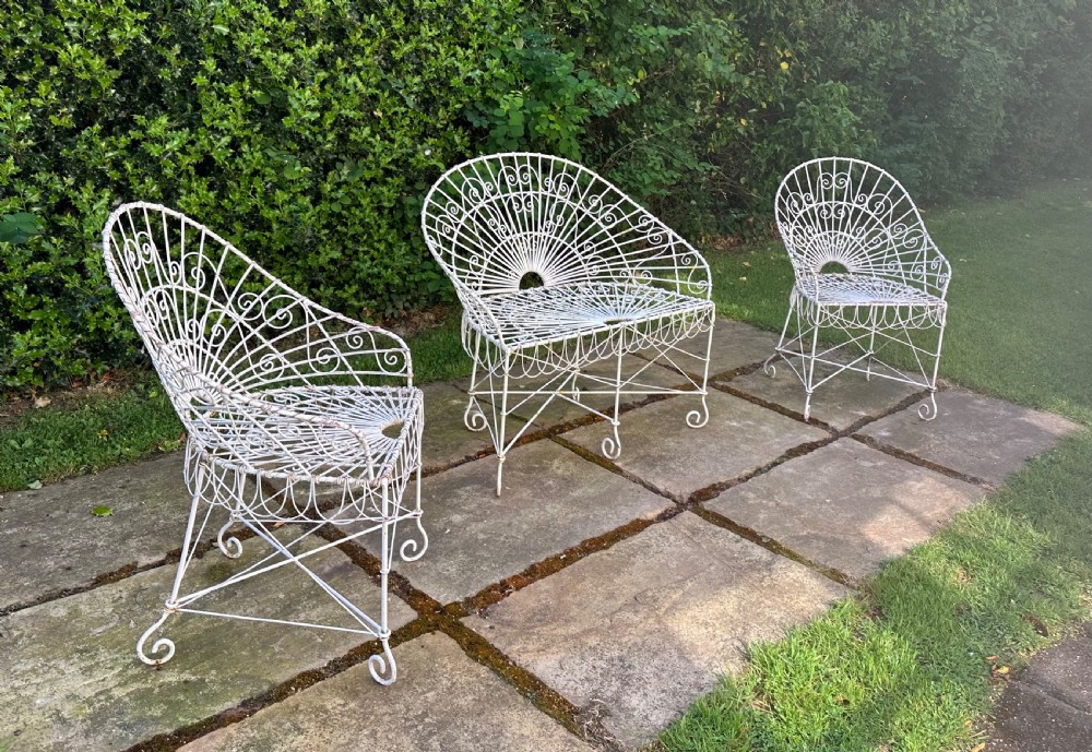A three-piece white painted wrought iron wirework garden set featuring a bench and two matching armchairs with arched fan-back designs.