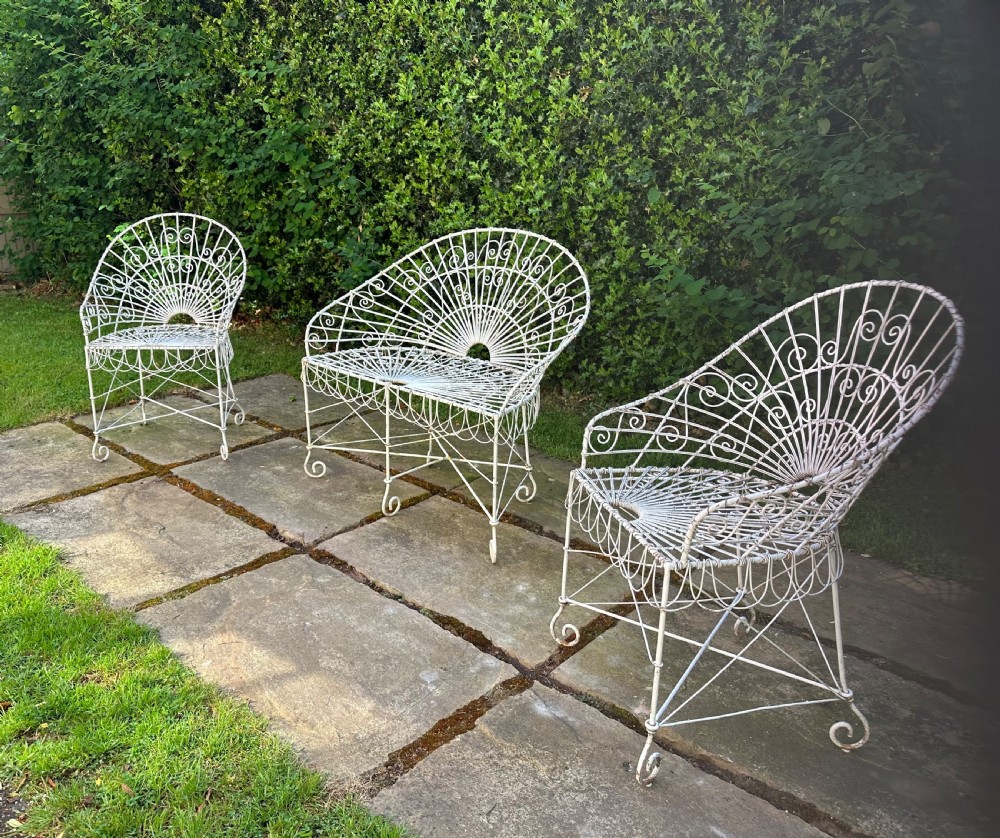 A three-piece white painted wrought iron wirework garden set featuring a bench and two matching armchairs with arched fan-back designs. View III
