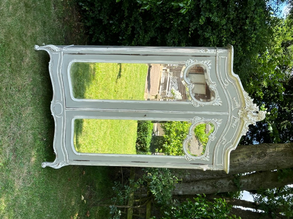 A grey and off-white painted French armoire featuring double mirrored doors and an ornate carved Rococo cresting. View II