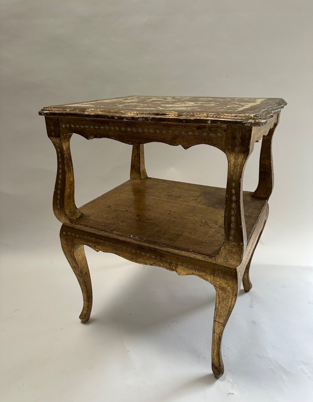A two-tiered Italian Florentine side table with a distressed gold leaf finish, cabriole legs, a scalloped apron, and decorative top surface detailing. View IV