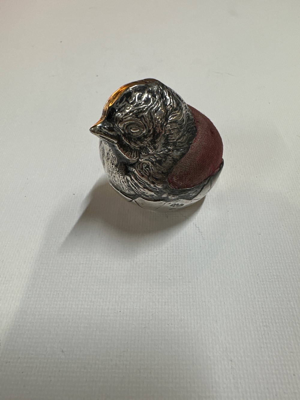 An Edwardian sterling silver novelty pin cushion modelled in the form of a chick hatching from an egg with a dark red velvet insert.