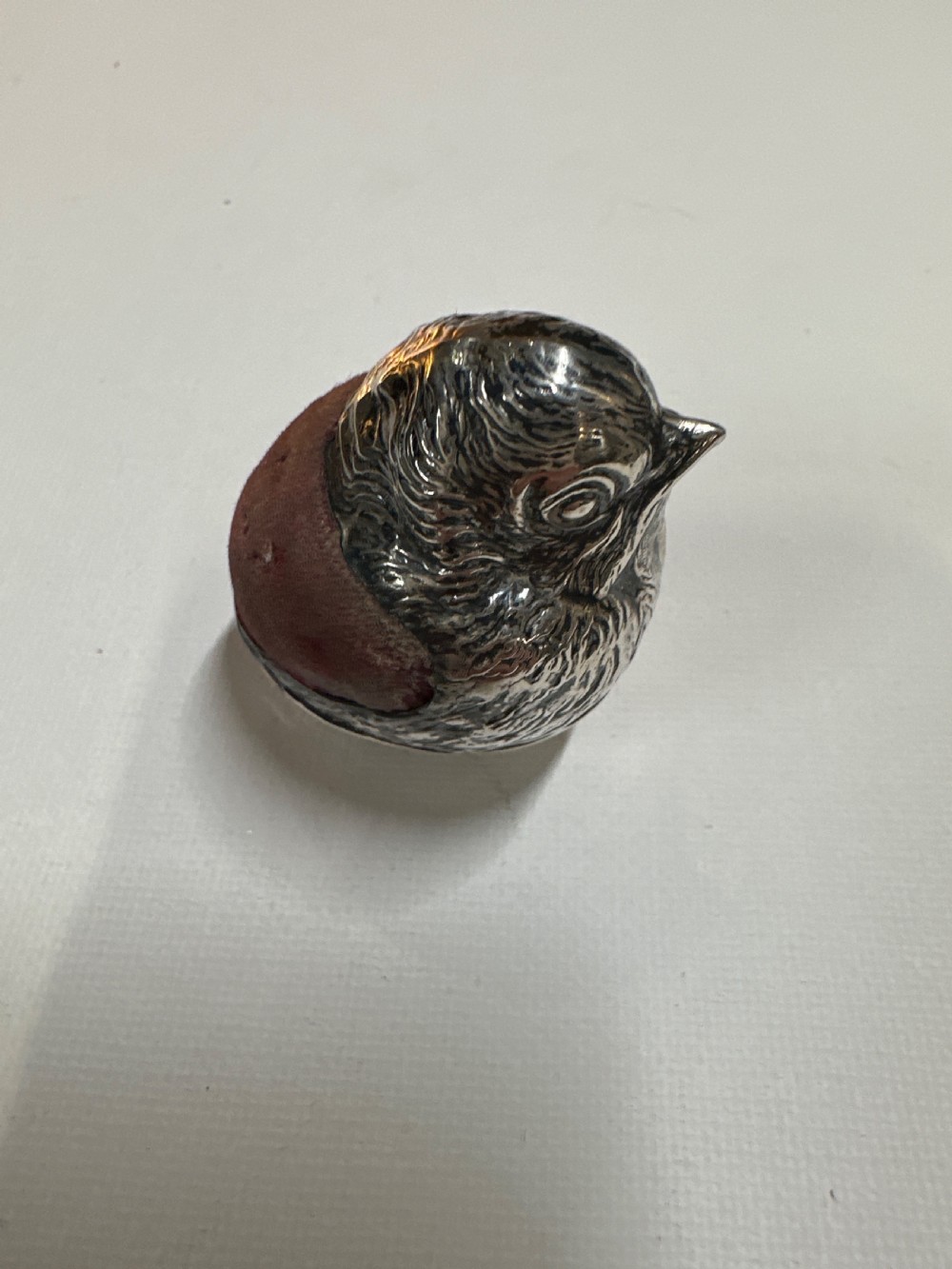 An Edwardian sterling silver novelty pin cushion modelled in the form of a chick hatching from an egg with a dark red velvet insert. View II