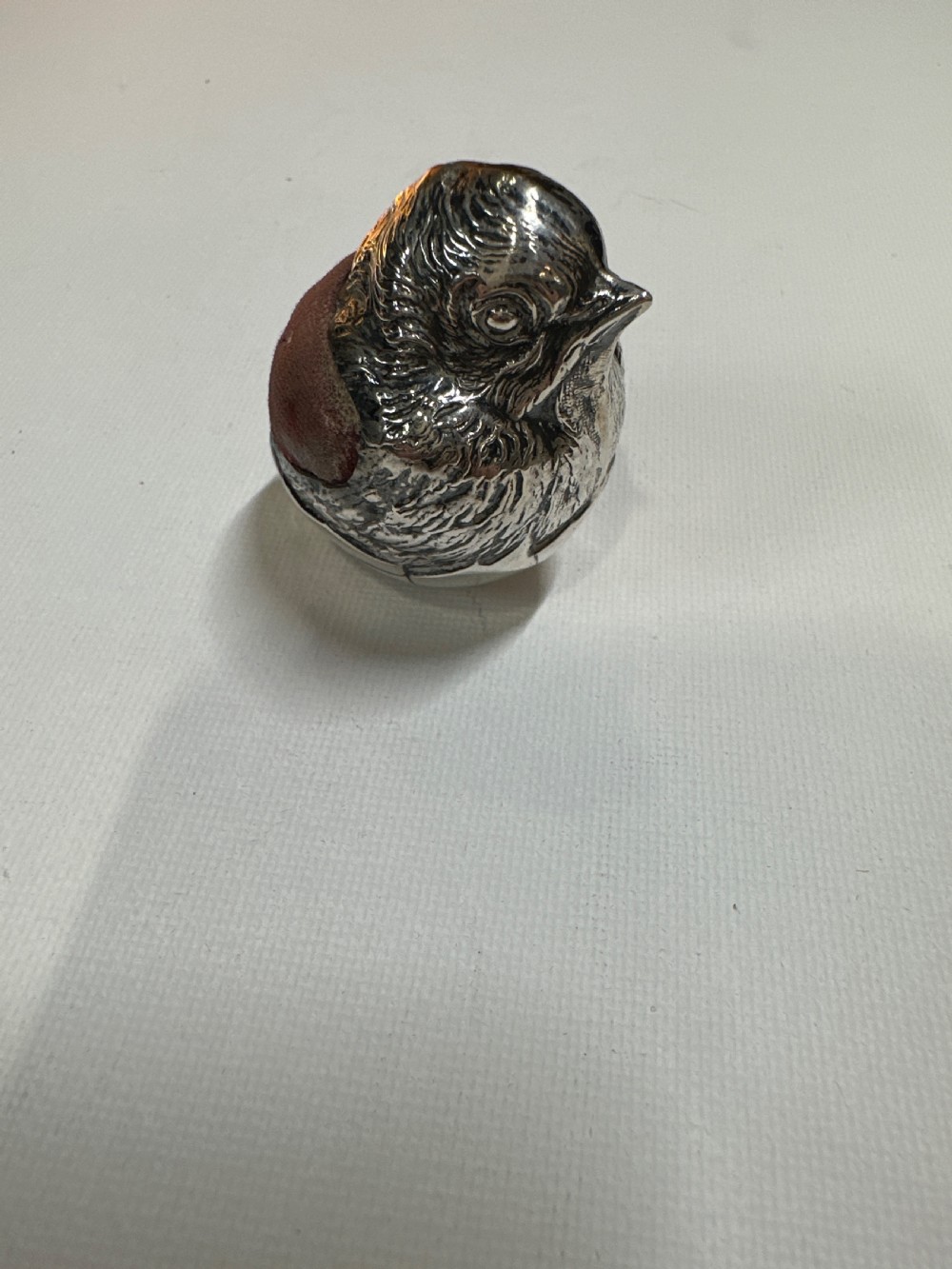 An Edwardian sterling silver novelty pin cushion modelled in the form of a chick hatching from an egg with a dark red velvet insert. View IV