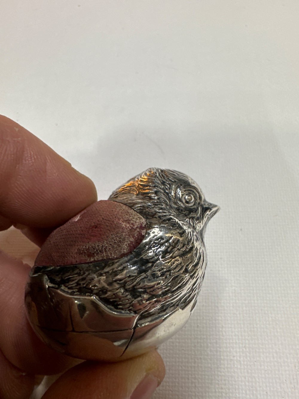 An Edwardian sterling silver novelty pin cushion modelled in the form of a chick hatching from an egg with a dark red velvet insert. View VI