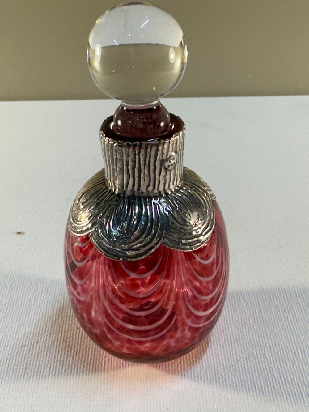 A patterned red glass perfume bottle featuring an embossed Irish silver collar and a round clear glass stopper. View II