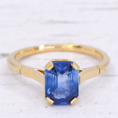 fig 2. A yellow gold solitaire ring featuring an emerald-cut blue sapphire secured in a corner-claw setting.