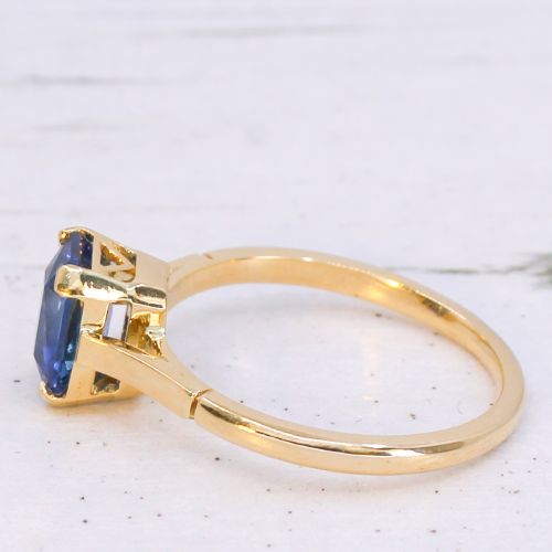 fig 3. A yellow gold solitaire ring featuring an emerald-cut blue sapphire secured in a corner-claw setting.