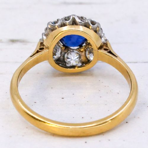 A yellow gold vintage ring featuring a central round blue sapphire encircled by a halo of brilliant-cut diamonds. View V