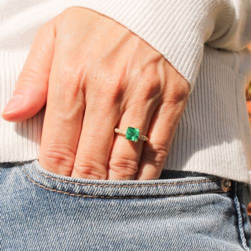 fig 1. A yellow gold ring featuring a central square-cut green emerald held in a four-prong setting, accented by three small round diamonds on each shoulder.