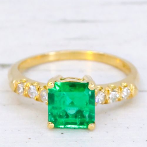 fig 2. A yellow gold ring featuring a central square-cut green emerald held in a four-prong setting, accented by three small round diamonds on each shoulder.