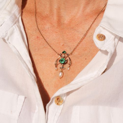 fig 1. An Art Nouveau openwork gold pendant featuring a central round green emerald, diamond accents, and hanging natural pearl drops.