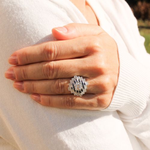 fig 1. An Art Deco diamond and sapphire cluster ring featuring a central brilliant-cut diamond surrounded by geometric borders of blue sapphires and smaller diamonds.