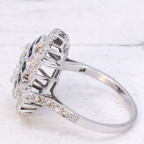fig 3. An Art Deco diamond and sapphire cluster ring featuring a central brilliant-cut diamond surrounded by geometric borders of blue sapphires and smaller diamonds.