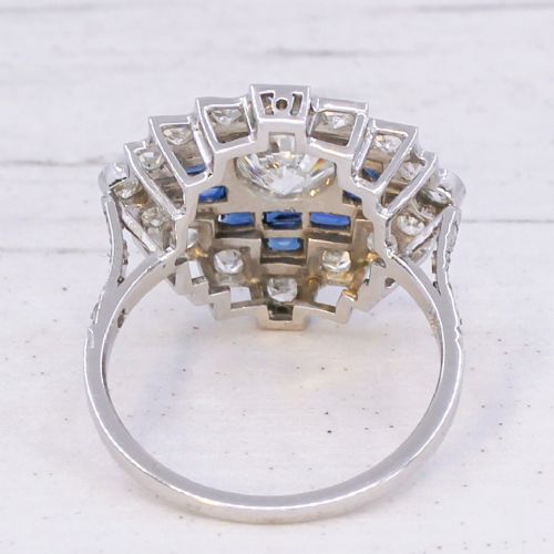 fig 4. An Art Deco diamond and sapphire cluster ring featuring a central brilliant-cut diamond surrounded by geometric borders of blue sapphires and smaller diamonds.