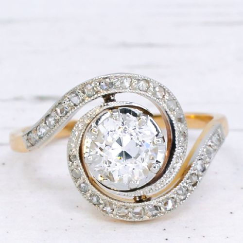 fig 2. An antique Edwardian diamond ring featuring a central old cut diamond wrapped in a platinum-faced swirl setting studded with small accent diamonds on a yellow gold band.