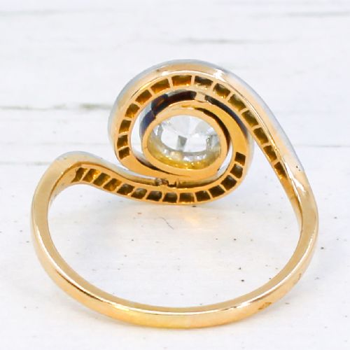 fig 4. An antique Edwardian diamond ring featuring a central old cut diamond wrapped in a platinum-faced swirl setting studded with small accent diamonds on a yellow gold band.