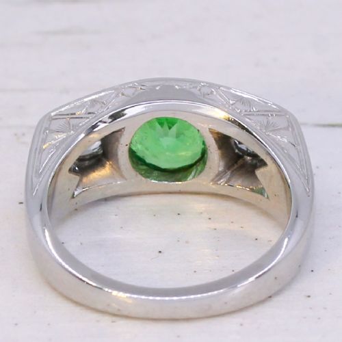 A white metal ring featuring a central round green tsavorite garnet flanked by two old cut diamonds set within a carved band. View V