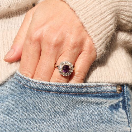 fig 1. An antique cluster ring featuring a central oval purple-red ruby surrounded by ten old cut diamonds in a scalloped white metal setting.