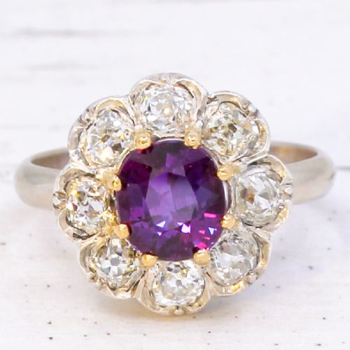 fig 2. An antique cluster ring featuring a central oval purple-red ruby surrounded by ten old cut diamonds in a scalloped white metal setting.