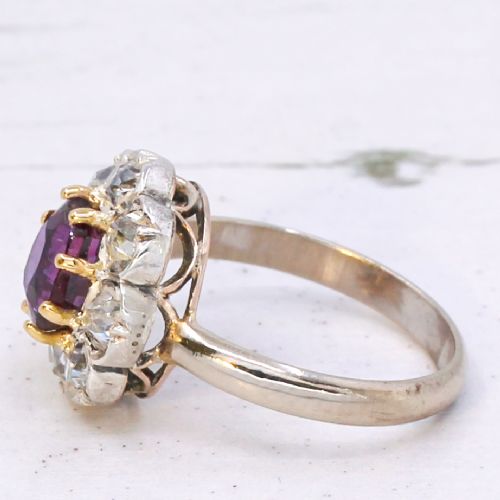 fig 3. An antique cluster ring featuring a central oval purple-red ruby surrounded by ten old cut diamonds in a scalloped white metal setting.