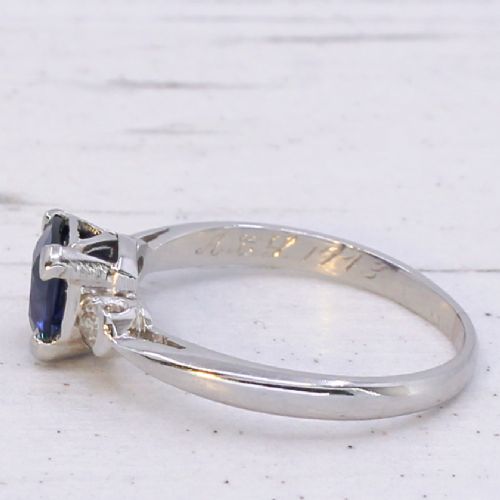 fig 4. A platinum ring featuring a central cushion-cut blue sapphire held in a claw setting, flanked by a small round diamond on each shoulder.