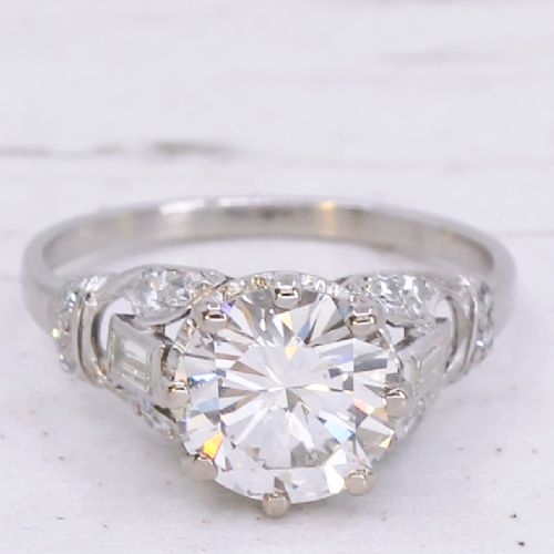 fig 2. A vintage mid-century platinum engagement ring featuring a central round brilliant cut diamond flanked by baguette and round accent stones.