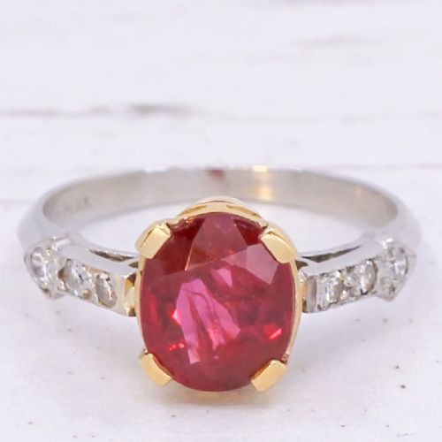 fig 2. A vintage Art Deco solitaire ring featuring an oval red ruby in a gold setting on a silver-toned metal band with diamond-set shoulders.