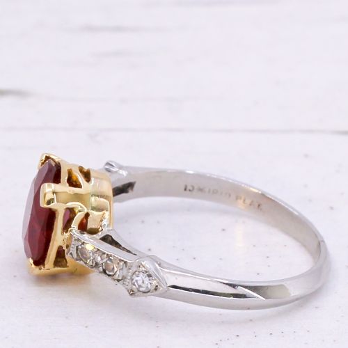 fig 3. A vintage Art Deco solitaire ring featuring an oval red ruby in a gold setting on a silver-toned metal band with diamond-set shoulders.