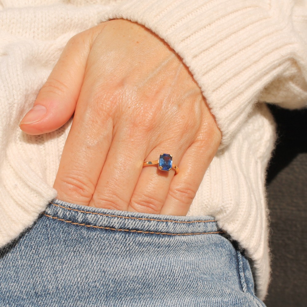 A yellow gold solitaire ring featuring an emerald-cut blue sapphire secured in a corner-claw setting. View II